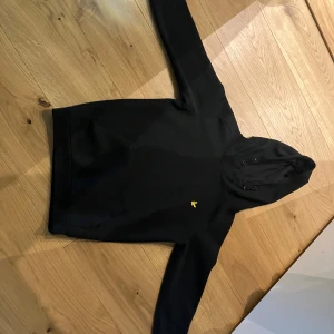 Svart hoodie från Lyle & Scott - Säljer en stilren svart hoodie från Lyle & Scott med deras ikoniska gula logotyp på bröstet. Perfekt för en avslappnad look. Passar åldern 11-12 om jag får säga det själv eller helt enkelt om du är runt 155-165