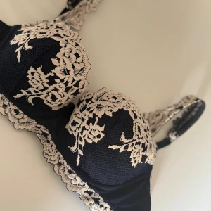 Marinblå spets-bh med blommigt mönster - Elegant marinblå bh med vacker beige/vit spets och blommigt mönster. Perfekt för att känna sig extra fin under kläderna. Axelbanden är justerbara och har också spetsdetaljer. Säljer eftersom jag söker efter en annan modell. Den är använd minst 3gånger!!🫶🏼🙏🏼💞