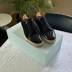 Lanvin DBB1 uk 6 svart - Snygga svarta sneakers med en kombination av mocka och lackdetaljer (Lanvin DBB1). Skorna har en klassisk snörning och en vit sula som ger en stilren kontrast. Perfekta för en trendig look. 