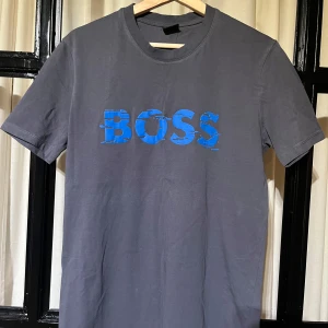 Grå t-shirt med blå text från Boss - It’s not washed out, it’s that style T-shirt, needs ironing or washing again. 