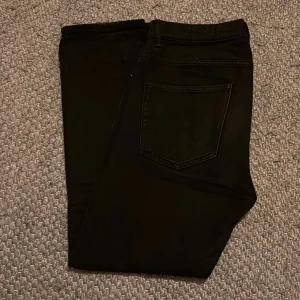 Svarta jeansbyxor - Snygga svarta jeansbyxor med en klassisk femficksdesign. De har en rak passform och är perfekta för en stilren look. Byxorna har hällor för bälte och en knappstängning framtill.