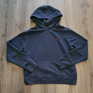 Mörkblå hoodie från Ralph Lauren - Säljer en snygg mörkblå hoodie från Ralph Lauren i storlek xl men sitter som S/M. Den har en klassisk design med en liten röd broderad logga på bröstet. Perfekt för både höst och vinter, och den är superbekväm att ha på sig. Passar perfekt för en laidback stil!