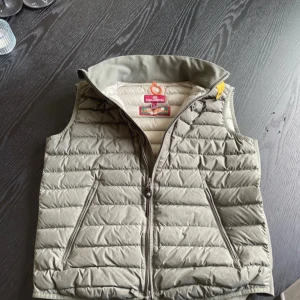 Beige dunväst från Parajumpers - Säljer en snygg beige dunväst från Parajumpers. Västen har en dragkedja framtill och är superlätt, perfekt för lager på lager. Den har en stilren design med två fickor framtill och en orange ögla i nacken. Passar perfekt för kyliga dagar!
