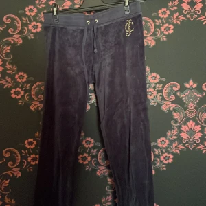 Mörkblå mjukisbyxor från Juicy Couture - Snygga mörkblå mjukisbyxor från Juicy Couture med glittrande JC-logga på höger sida. Byxorna har en bekväm passform med snörning i midjan och fickor med knappar. Perfekta för en avslappnad stil. köpta på plick aldrig användna av mig. tecken på användning men inga defekter.