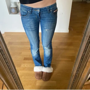 Blå jeansbyxor från Diesel - Snygga blå jeansbyxor från Diesel med slitna detaljer och dragkedja på bakfickan. De har en låg midja och en tight passform som ger en modern look. Perfekta för en avslappnad stil. Köpta här på plick men är o bra skick, säljer pga av att de är lite stora. Lånade bilder!