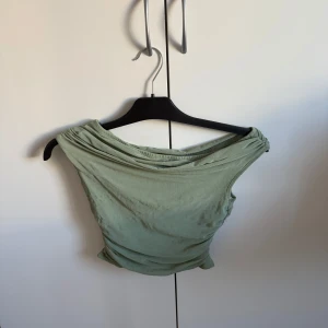 Grön offshoulder topp - Snygg grön offshoulder topp med draperad design. Perfekt för en stilren look. Passar bra till både jeans och kjol.