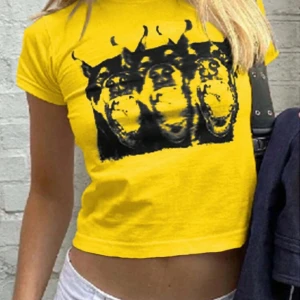 Gul croppad t-shirt med tryck - Snygg gul croppad t-shirt med ett coolt svart tryck av tre djurhuvuden. Perfekt för en avslappnad stil med en twist. Kortärmad och iögonfallande design.