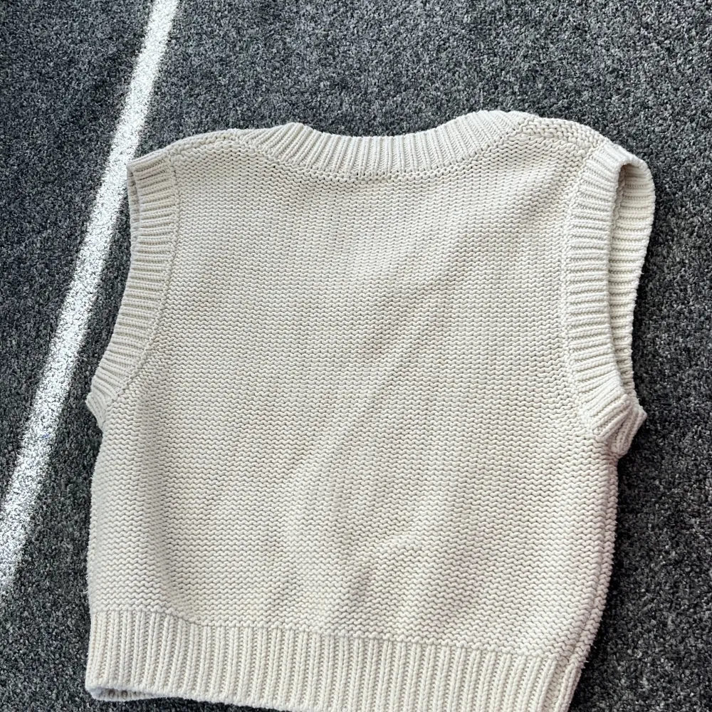 Säljer en stilren beige stickad väst från Lindex för barn. Västen har en v-ringad design och ribbade kanter som ger en klassisk look. Perfekt för lager-på-lager under kyligare dagar.. Takit.