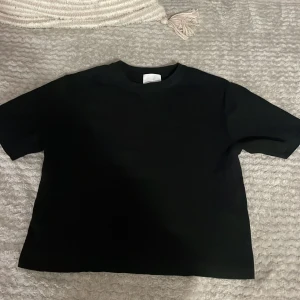 Svart t-shirt från H&M - Säljer en klassisk svart t-shirt från H&M i storlek XS. Den har en enkel design med korta ärmar och rund halsringning. Perfekt basplagg för garderoben.
