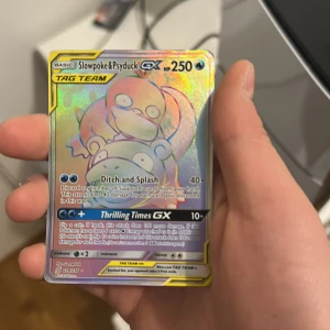 Pokémonkort Slowpoke & Psyduck GX - Säljer ett holografiskt Pokémonkort med Slowpoke & Psyduck GX från TAG TEAM-serien. Kortet har en glansig yta och visar de två Pokémon-karaktärerna i en färgglad design. Perfekt för samlare eller Pokémon-fans!