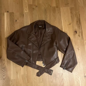 Brun skinnjacka från Bianca x Nelly - Snygg brun skinnjacka från Bianca x Nelly med en croppad design. Jackan har dragkedja och bälte.