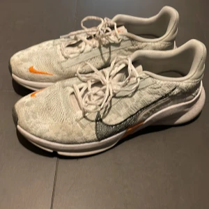 Nike löparskor i vitt och orange - Säljer ett par Nike löparskor i vitt med orange detaljer. Skorna har en snygg design med snörning och en bekväm passform. Perfekta för löpning och träning.