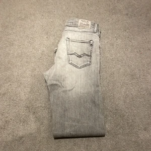 Grå jeans från Replay - Snygga grå jeans från Replay med klassisk ficksdesign och dragkedjegylf. Perfekta för en stilren look. Märkesdetaljer på bakfickan och linningen ger en extra touch. 