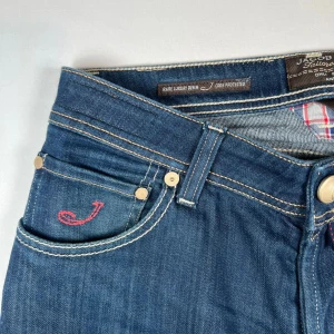 Jacob Cohen jeans - Snygga blå jeansbyxor från Jacob Cohen med en cool röd broderad 'J' på fickan. Byxorna har en klassisk femficksdesign och kontrastsömmar som ger en stilren look. Perfekta för en avslappnad stil. Bla bla skiti vad AI säger. Det här är feta jeans, pris går att diskuteras. 