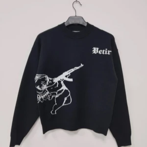 Svart tröja med ängelmotiv - Snygg svart tröja från Vetir med ett unikt ängelmotiv som håller i ett gevär på framsidan. Baksidan har texten 'MM.XX.IV' och ett vingmotiv. Perfekt för en cool och edgy stil.