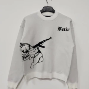 Vit tröja med ängelmotiv från Vetir - Säljer en cool vit tröja från Vetir med ett unikt ängelmotiv som håller ett gevär på framsidan. Baksidan har romerska siffror och en vinge. Tröjan har långa ärmar och en rund halsringning. Perfekt för dig som vill sticka ut!