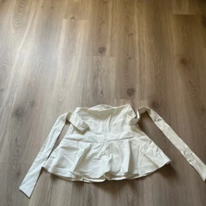 Vit kjol med knytband - Säljer en stilren vit kjol med knyt till rosett i midjan. Perfekt för en elegant look. Kjolen har en lätt volangdetalj vid nederkanten.