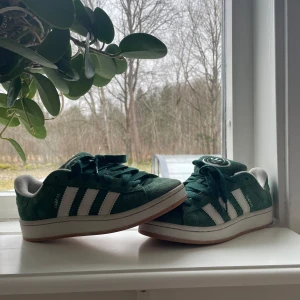 Gröna Adidas campus - Snygga gröna Adidas campus sneakers med klassiska vita ränder och snörning. Skorna har en stilren design med vit sula och Adidas-logga på hälen. Perfekta för en avslappnad stil.