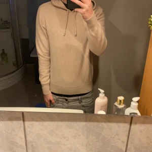 Beige cashmere hoodie från Sayless - Säljer en supermjuk och stilren beige hoodie från Sayles i lyxig cashmere. Perfekt för att hålla sig varm och bekväm under kyliga dagar. Den har en klassisk design med dragsko i huvan och ribbade muddar vid ärmslut och nederkant. Storlek S men mer åt xs hållet