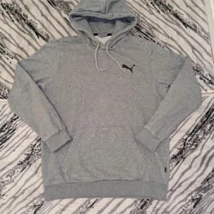 Grå hoodie från Puma - Säljer en stilren grå hoodie från Puma med klassisk känguruficka och justerbar huva. Perfekt för en avslappnad stil. Den har ett svart Puma-logotyptryck på bröstet.