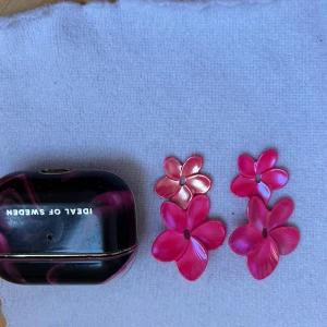 Rosa blommiga örhängen  - Snygga rosa örhängen i form av blommor. De har en glansig yta och kommer i olika storlekar för en unik look. Perfekta för att lägga till en färgklick till din outfit.