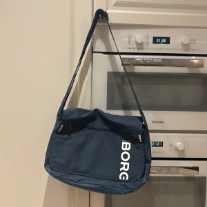 Tennisväska från Björn Borg - Snygg blå axelväska från Björn Borg med justerbar axelrem och praktiska fack. Väskan har en dragkedja och ett quiltat mönster på baksidan. Perfekt för att bära med sig det nödvändigaste i vardagen.