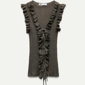 Grön ribbad topp från Zara - Snygg grön ribbad topp från Zara med volangdetaljer längs ärmarna och fram. Toppen har en knytning framtill och är ärmlös, perfekt för en chic look. Säljer då den inte satt på mig som jag ville