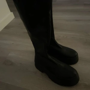 Svarta höga stövlar - Snygga svarta stövlar i skinn med hög skaft. Perfekta för en stilren look. De har en rund tå och en robust sula som ger bra grepp.
