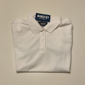 Vit pikétröja från James Harvest - Säljer en helt ny stilren vit pikétröja från James Harvest med svarta detaljer längs sidorna. Tröjan har korta ärmar och tre knappar framtill. Perfekt för en stilig look! Nypris: Cirka 500kr men jag säljer den för halva priset!