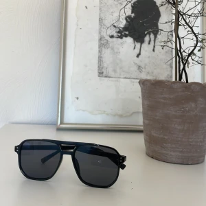 Svarta solglasögon med fyrkantig form - Snygga svarta solglasögon med en modern fyrkantig design. De har en robust ram och mörka linser som ger ett stilrent intryck. Perfekta för soliga dagar och en cool look.