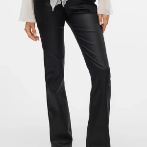 Svarta byxor i skinnimitation - Trendiga Snygga svarta byxor i skinnimitation med en bootcut-stil. De har en klassisk femficksdesign och stängs med dragkedja och knapp. Perfekta för en trendig look. använda ett fåtal gånger men är som nya.