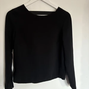 Svart långärmad blus - Snygg svart långärmad blus med en elegant öppen rygg. Perfekt för en stilren look. Passar bra till både jeans och kjol.