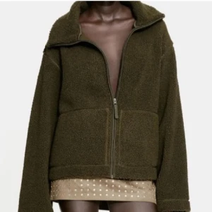 grön teddyjacka hm - Säljer en mysig olivgrön teddyjacka med dragkedja framtill. Jackan har en avslappnad passform och långa ärmar, perfekt för kyligare dagar. Den är både stilren och bekväm, ett måste i garderoben!