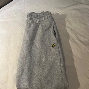 Grå mjukisbyxor från Lyle & Scott - Säljer ett par grå mjukisbyxor från Lyle & Scott med elastisk midja och en liten logga på sidan. Perfekta för en avslappnad stil.