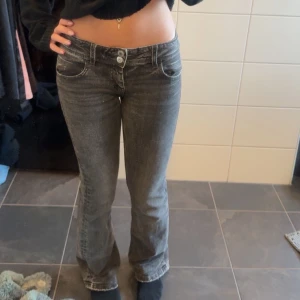 Grå jeans - Jättesnygga grå/svarta jeans med väldigt låg midja och bootcut. Byxorna har en klassisk femficksdesign och stängs med en dragkedja och knapp framtill. 