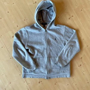 Ralph Lauren zip hoodie - Hej, säljer en grå Ralph Lauren zip hoodie. Den är i bra skick. Storlek L i barn storlek vilket motsvarar XS. Hör av er vid funderingar. MVH Jack Von Grisch.