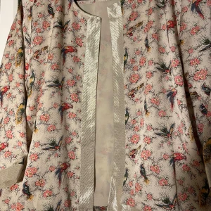 Blommig kimono från Lollys Laundry - Säljer en vacker kimono från Lollys Laundry i storlek M. Den är beige med ett färgglatt blommönster och fåglar. Tillverkad i 100% polyester, perfekt för en stilfull look. 🦜🌸