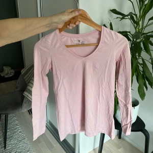 Rosa långärmad topp - Säljer en söt rosa långärmad topp med v-ringning. Perfekt för en avslappnad stil och enkel att matcha med olika outfits. Passar bra till både jeans och kjol.