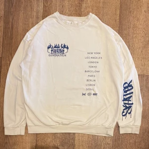 Vit Sweatshirt från H&M Storlek 170-XS - Säljer en vit sweatshirt från H&M med tryck av olika städer på framsidan och blå text på ärmen. Tröjan har långa ärmar och en rund halsringning. Perfekt för en avslappnad stil. Storlek 170 - Xs. Snabb Leverans!