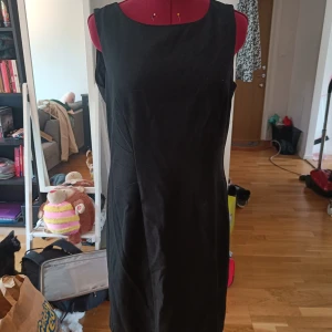 Svart ärmlös kortklänning - En klassisk svart ärmlös klänning med rund halsringning och figurnära passform. Klänningen har dragkedja i ryggen och är enkel men stilren, perfekt för dig som gillar minimalistisk stil. Passar lika bra med sneakers som med klackar.