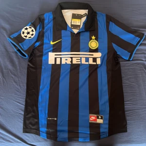 Inter Ronaldo 9 Nike fotbollströja S - Inter Milan fotbollströja med Ronaldo 9 på ryggen. Klassisk blå och svart randig design, Champions League-märke på ärmen och broderat Inter-emblem med stjärna. Tillverkad i lätt och ventilerande polyester, perfekt för match eller samling.