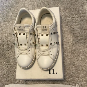 Valentino Rockstud vita sneakers - Snygga vita Valentino Rockstud sneakers i skinn med ikoniska silverfärgade nitar och klassisk snörning. Skorna har rund tå och platt sula, samt coola detaljer som gör dem till ett statement-piece. Perfekta för dig som vill sticka ut med en lyxig Grisch stil. Vid frågor de bara att skicka ett dm 😁