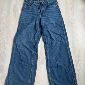 Blå wide jeans från Bershka, strl 34 - Säljer ett par blå jeans från Bershka i storlek 34. Modellen är wide leg med hög midja och klassisk femficksdesign. Jeansen är i denim med dragkedja och knapp framtill. Perfekta för en avslappnad och trendig look.
