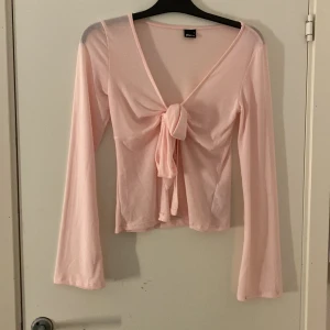Ljusrosa knyt-topp från Gina Tricot - Supersöt ljusrosa knyt-topp från Gina Tricot med långa ärmar och knyt framtill. Tunn och mjuk i materialet, perfekt för lager på lager eller som den är. Djup v-ringning och feminin passform som ger en trendig vibe.
