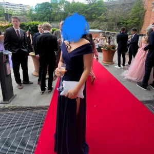 Marinblå långklänning med slits - Elegant marinblå långklänning med offshoulder och v-ringad överdel. Klänningen har en hög slits på ena sidan som ger en snygg och modern look. Perfekt för bal eller fest. Materialet känns mjukt och följsamt mot kroppen.