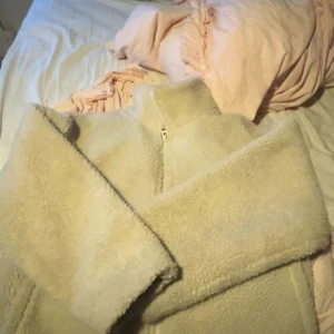 Beige teddyjacka från Carin Wester - Supermjuk och mysig beige teddyjacka från Carin Wester. Jackan har hög krage, dragkedja framtill och är tillverkad i fluffigt teddy-material som håller dig varm under kyliga dagar. Perfekt för dig som gillar en chill och trendig look.