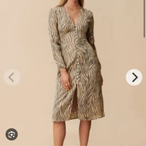 Zebramönstrad långklänning Adoore - Snygg långklänning med zebramönster i beige och svart. Klänningen har v-ringning, långa ärmar och knappar hela vägen framtill. Perfekt för dig som vill sticka ut med en trendig look.