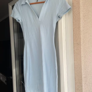 Ljusblå kortklänning från NLY Trend - Supersöt ljusblå kortklänning från Ivy Trend i mjuk bomull. Klänningen har v-ringning, krage och korta ärmar. Enkel och stilren design som är lätt att matcha med sneakers eller sandaler. Perfekt för varma dagar när du vill känna dig både bekväm och snygg.