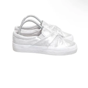 Silvriga slip-ons skor  - Glittriga slip-on sneakers i silver med snygg knutdetalj framtill. Oanvända då dem är för små på mig!! Jätte nice modell av skor till sommaren ☺️💖🤗
