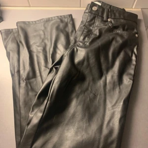 Svarta skinnbyxor med raka ben - Snygga svarta byxor i skinnimitation med raka ben och klassisk femficksmodell. Byxorna har bälteshällor, knapp och dragkedja framtill samt bakfickor. Perfekta för en edgy look och passar till allt.